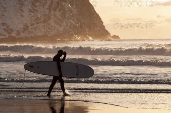 Surfer with surfboard under his arm on the beach of Unnstad, winter surfing, Lofoten Island