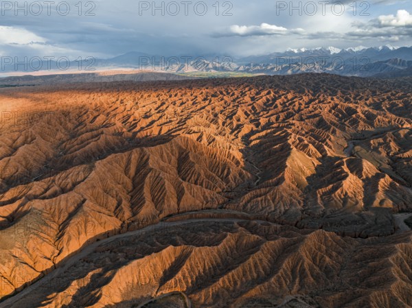 River bed runs through a landscape of eroded hills, badlands at sunset, mountain peaks of the Tian