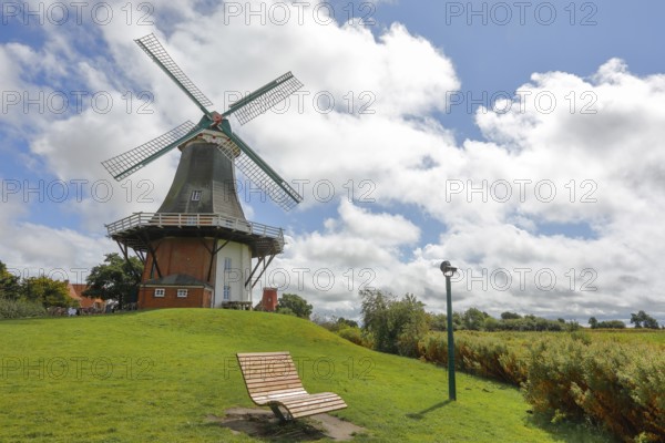 A windmill in front of a dramatic blue sky, surrounded by green meadows with a deckchair,