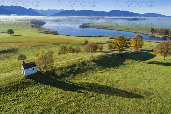 Aerial view of a small chapel in front of a lake, mountain landscape, autumn, sunny, Riegsee,