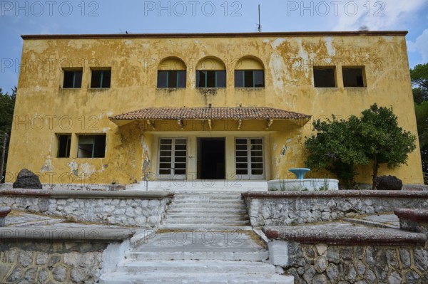An old yellow dilapidated building with a damaged façade and a staircase in the entrance, Italian