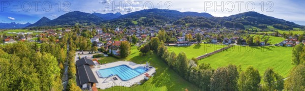 Panoramic view of a village with a swimming pool, surrounded by green meadows and forests, against