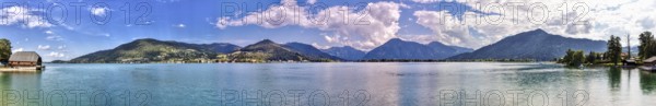 Clear water of a lake with surrounding mountains, on a sunny day with blue sky and white clouds,