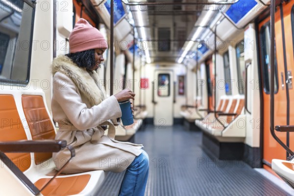 Passenger opening a reusable coffee cup while enjoying a quiet moment on a nearly empty subway