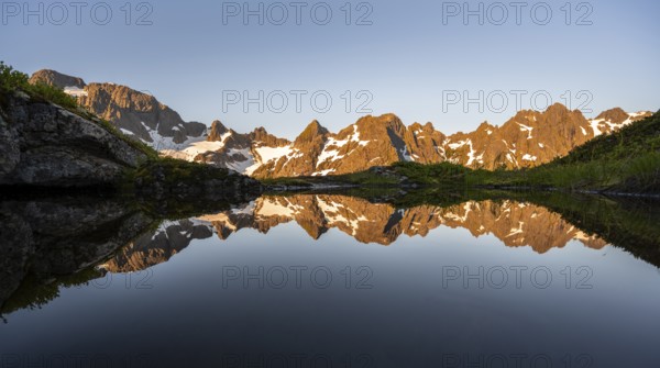Rocky mountain peaks reflected in a small pond, mountain landscape with alpenglow at sunrise, at
