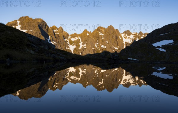 Rocky mountain peaks reflected in a small pond, mountain landscape with alpenglow at sunrise, at
