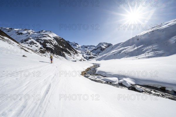 Ski tourer in the snow by a mountain stream in the Funtauna Valley, Sonnenstern, Graubünden Haute