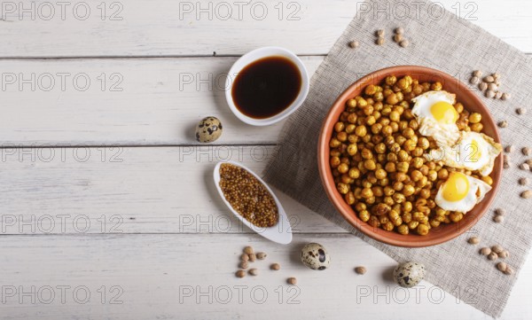 Fried chickpeas with quail eggs and spices in a clay plate on white wooden background, top view,