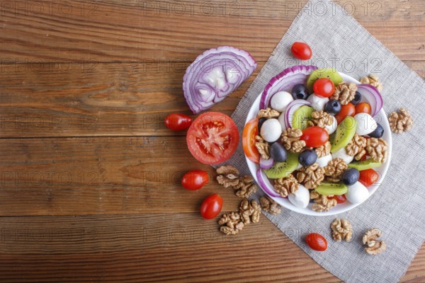 Salad with fresh cherry tomatoes, mozzarella cheese, olives, kiwi, onion and walnuts on brown