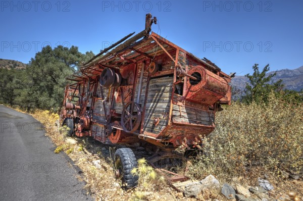 Dilapidated, rusted combine harvester next to the road under blue sky, wrecked vehicle, Crete,