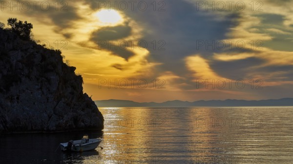 Atmospheric sunrise over the sea with cliffs and a boat, Mani Peninsula, Peloponnese, Greece,