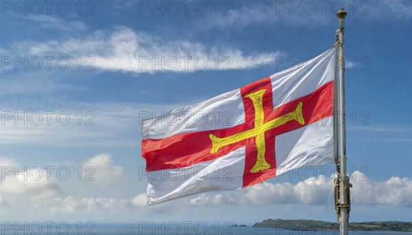 The flag of the Isle of Guernsey, Great Britain, flutters in the wind