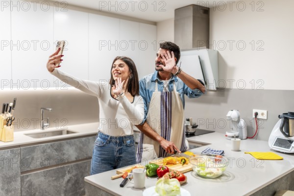 Young couple waving at the camera while preparing a healthy salad in their kitchen, making a video