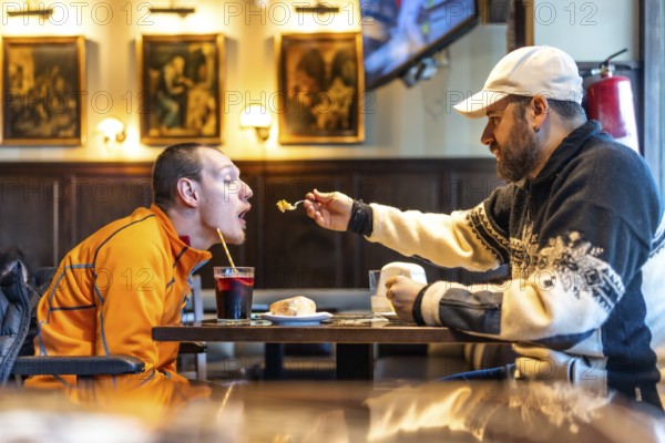Man feeding his disabled friend in a restaurant, showcasing genuine care and inclusivity while