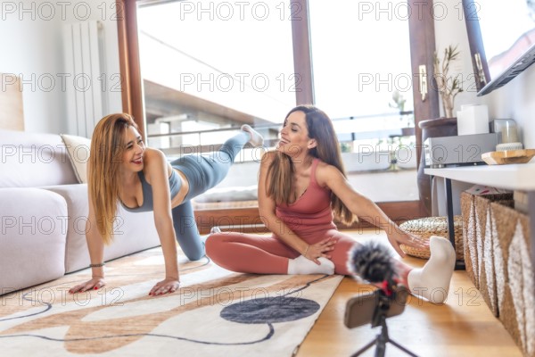 Two fitness trainers recording online yoga class at home using smartphone and microphone, promoting