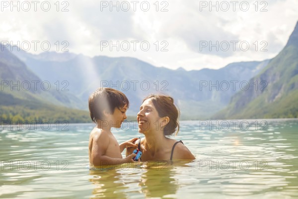 Mother and son enjoying summer holidays, playing in the refreshing water of lake bohinj, surrounded