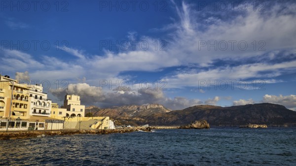 Morning light, coastal town with buildings by the sea and mountains in the background, Pigadia,