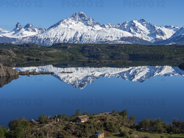 The snow-covered Mt. Cerro Castillo is reflected in a lake, small farm by the lake, Patagonia,