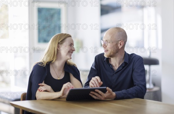 Symbolic photo. A woman and a man sit together at a table with a tablet and talk. Berlin, 13.08