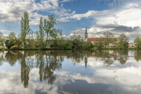 Huttenheim village reflected in a natural tree-lined river in spring. Bas Rhin, Alsace, France,