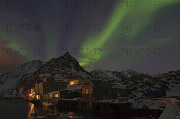 Night scene with northern lights in the sky, mountains in the background and illuminated houses on