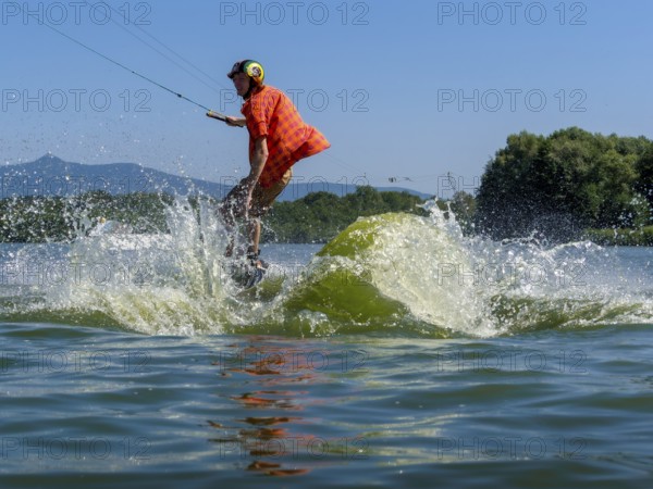 Young casual man with flapping shirt on wakeboard jumping into the lake, water ski and wakepark,