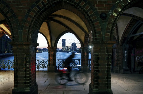 Bicycle rider to the sunrise at the Oberbaum Bridge, view through the arcades over the Spree to the