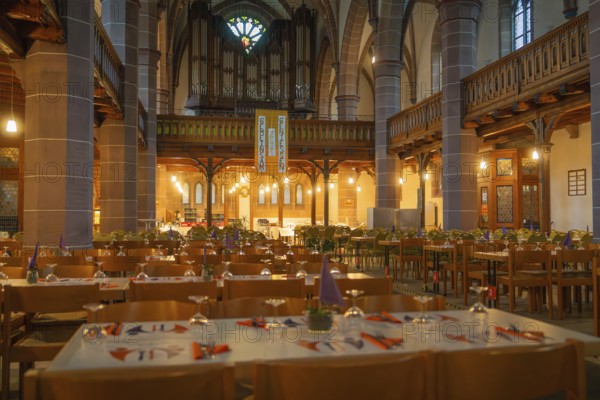 Several laid tables in a warmly lit church with organ in the background, Vesperkirche Calw, Black