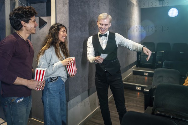 Young couple holding popcorn buckets while usher showing their seats in a movie theater, ready to