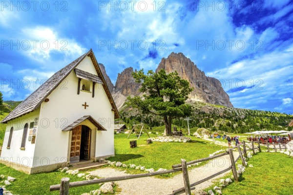 Tourists enjoying a sunny day at sella pass, with the chapel and the sassolungo group in the