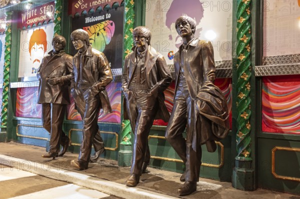 Four bronze statues depict people in motion in front of a decorated block, Liverpool