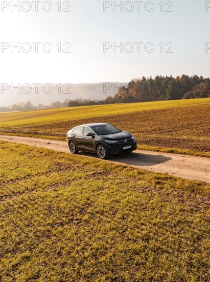 A car drives alone on a country lane, surrounded by golden fields under the sun, electric car VW