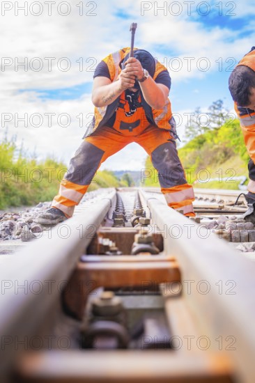 Two construction workers working on the rails, looking along the tracks in a rural setting, rail