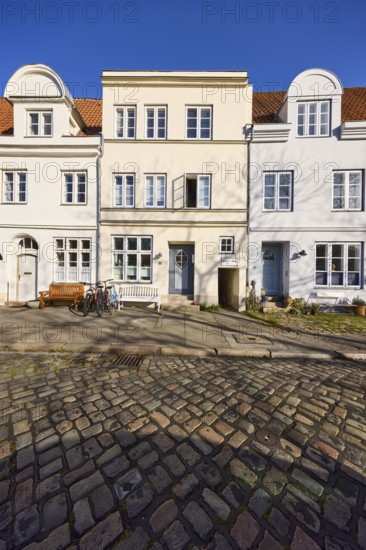 Historic houses, facades with windows, roofs with red roof tiles and dormers, cobblestone pavement,