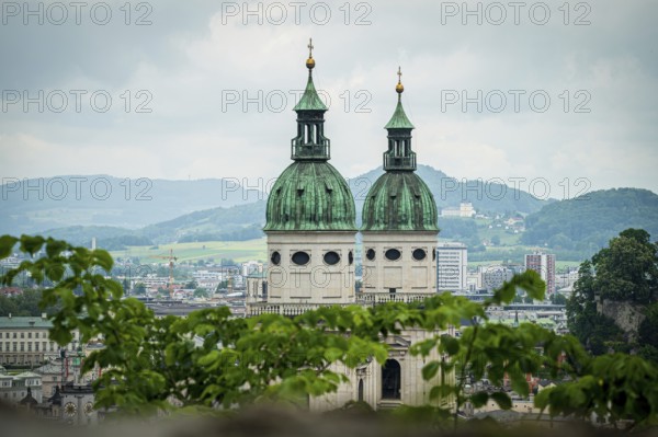 Two church towers with green roofs, framed by leaves, landscape in the background, Salzburg,