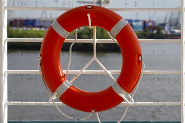 An orange lifebuoy hangs from a white railing with a view of a harbour, Hamburg, Germany, Europe