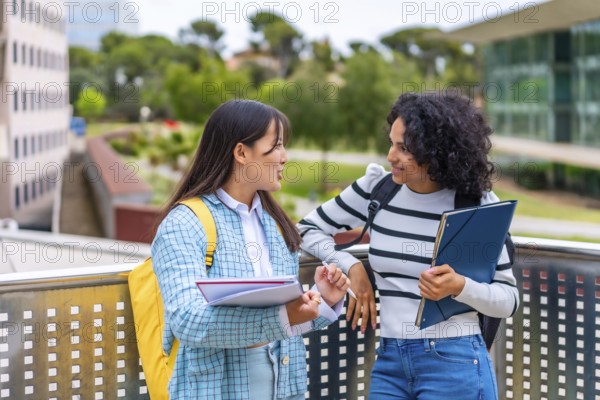 Two multi-ethnic female students reading and commenting notes standing outside the campus