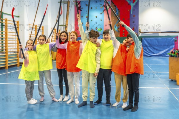 Group of cheerful students wearing colorful bibs raising hockey sticks and celebrating in school