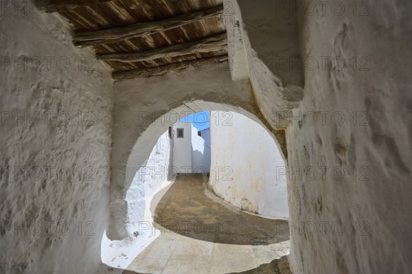 Arched passageway with wooden ceiling and white walls in a historic building, Chora, main town of