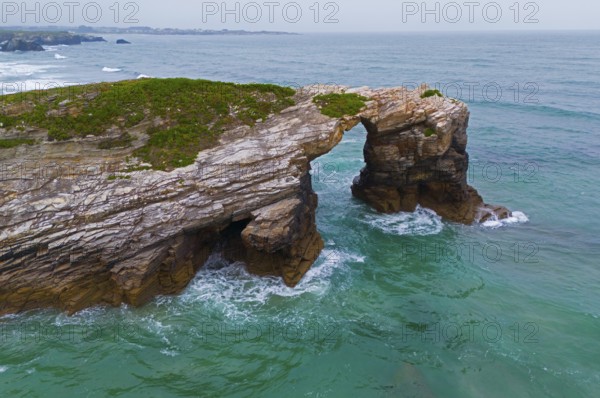 Rocky arch on the coast above the roaring ocean with green-blue water, aerial view, Praia das