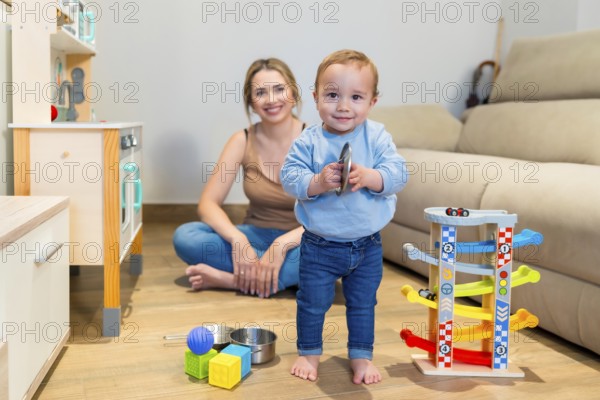 Adorable baby boy playing with a toy cymbal while mother sits on the floor, capturing a