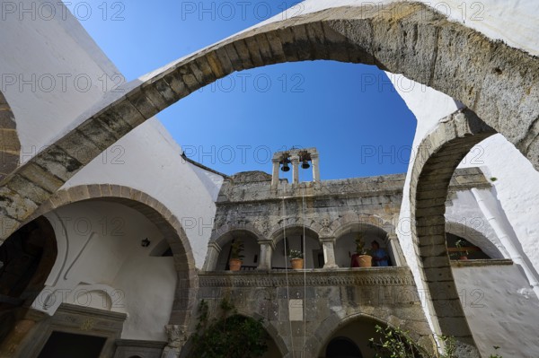 Historic monastery with stone arches and a bell tower under a blue sky, Inside the monastery, Agiou