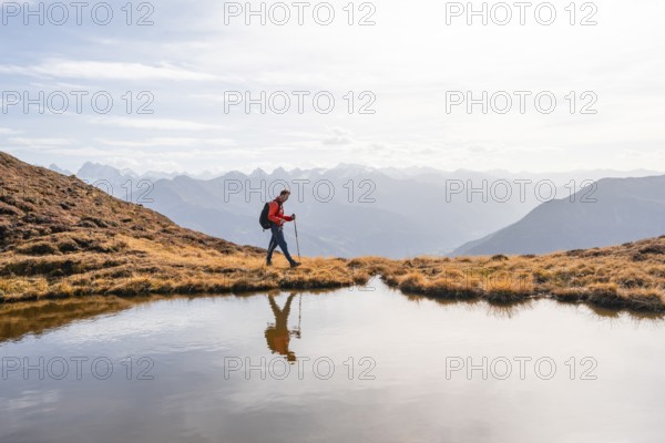 Mountaineer hiking with poles, reflected in a small mountain lake on the Krahberg, mountain