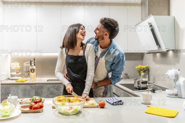 Young loving couple wearing aprons, preparing a healthy salad together in their modern kitchen,