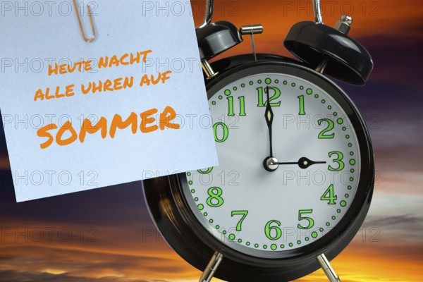 (Photomontage) Summer time changeover Symbolic image: Alarm clock in front of evening sky and text