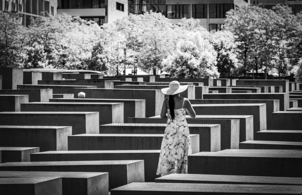 Black and white photograph, woman in summer dress amidst the Holocaust memorial steles at the