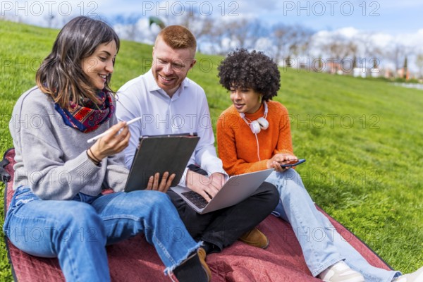 Three university students collaborating on a project, using a digital tablet and laptop while