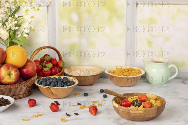 Muesli in a wooden bowl surrounded by ingredients, fruit, strawberries, blueberries, cornflakes,