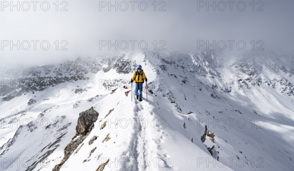 Mountaineer climbing up the narrow ridge of Piz Laviner, view of wintry mountain landscape, Grisons