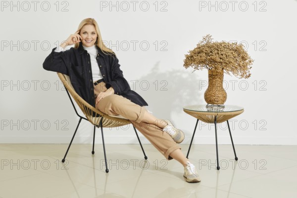 A cheerful woman poses comfortably in a stylish chair, her relaxed expression accentuated by the